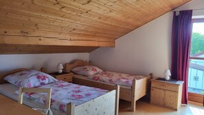 Une pièce avec deux lits en bois, une table de chevet en bois, une chaise et une fenêtre avec des rideaux.