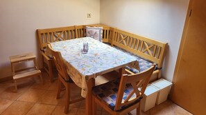 Un coin repas avec une table et un banc en bois, un petit tabouret en bois et un sol carrelé.