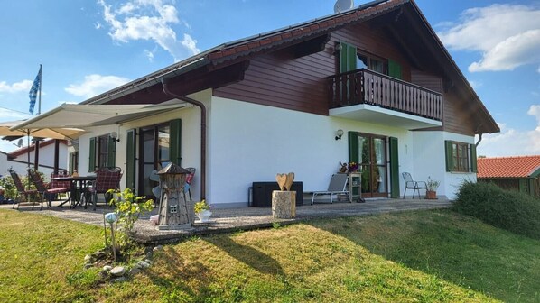 Une maison à deux étages dotée d’un balcon, d’un patio couvert et d’un petit jardin.