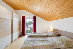 A bedroom with a sloped ceiling, a window with red curtains, and two beds with patterned bedding.