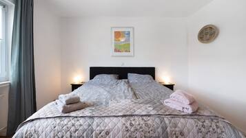 A bedroom with a bed, two bedside tables, a painting on the wall, and a round mirror.
