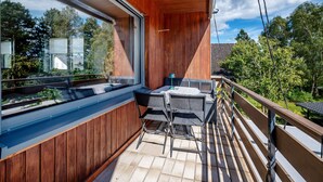 Un balcone con tavolo e sedie, rivestimento in legno e vista su alberi e una casa.