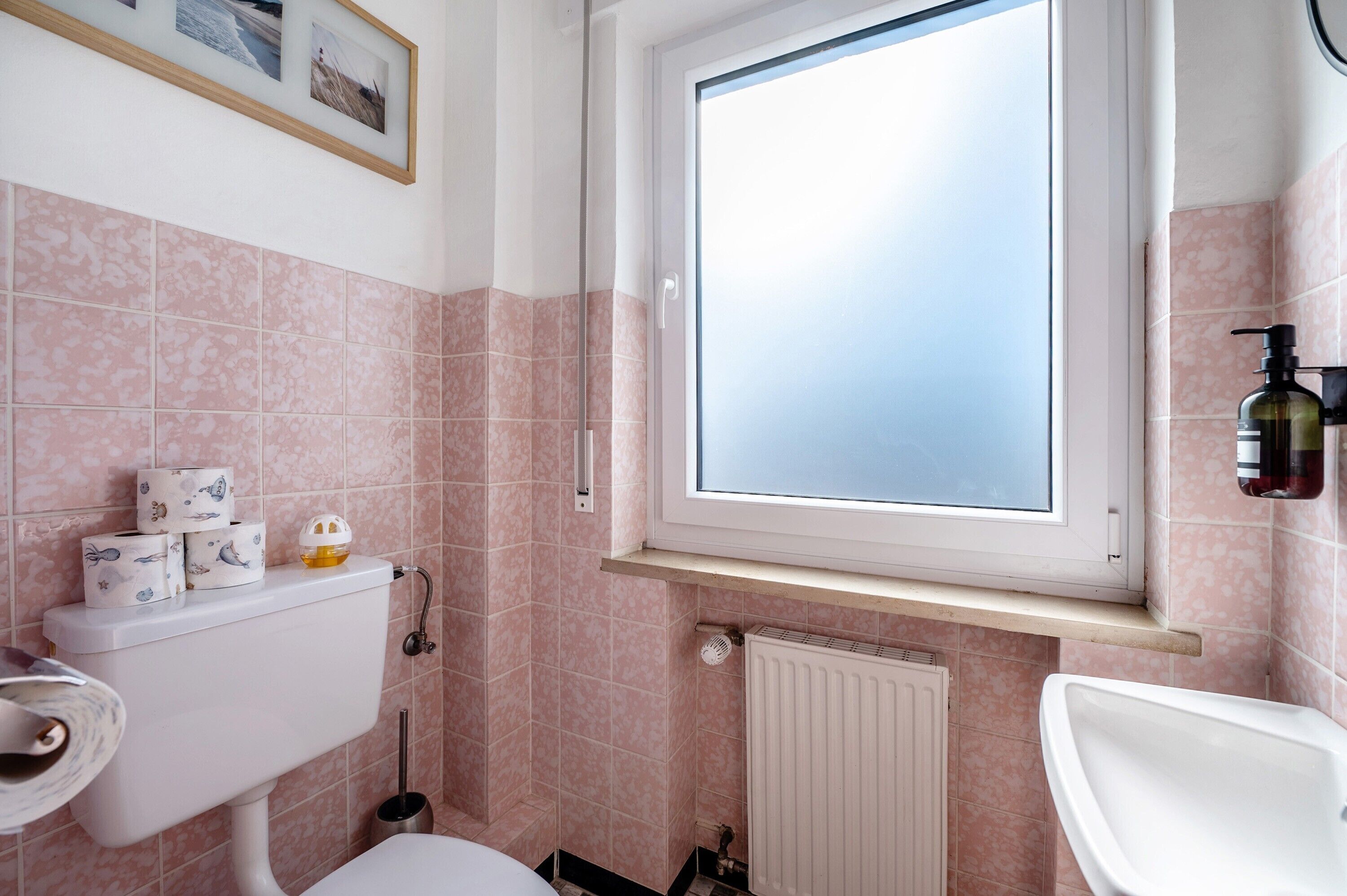 Een badkamer met toilet, wastafel, raam en roze tegels.