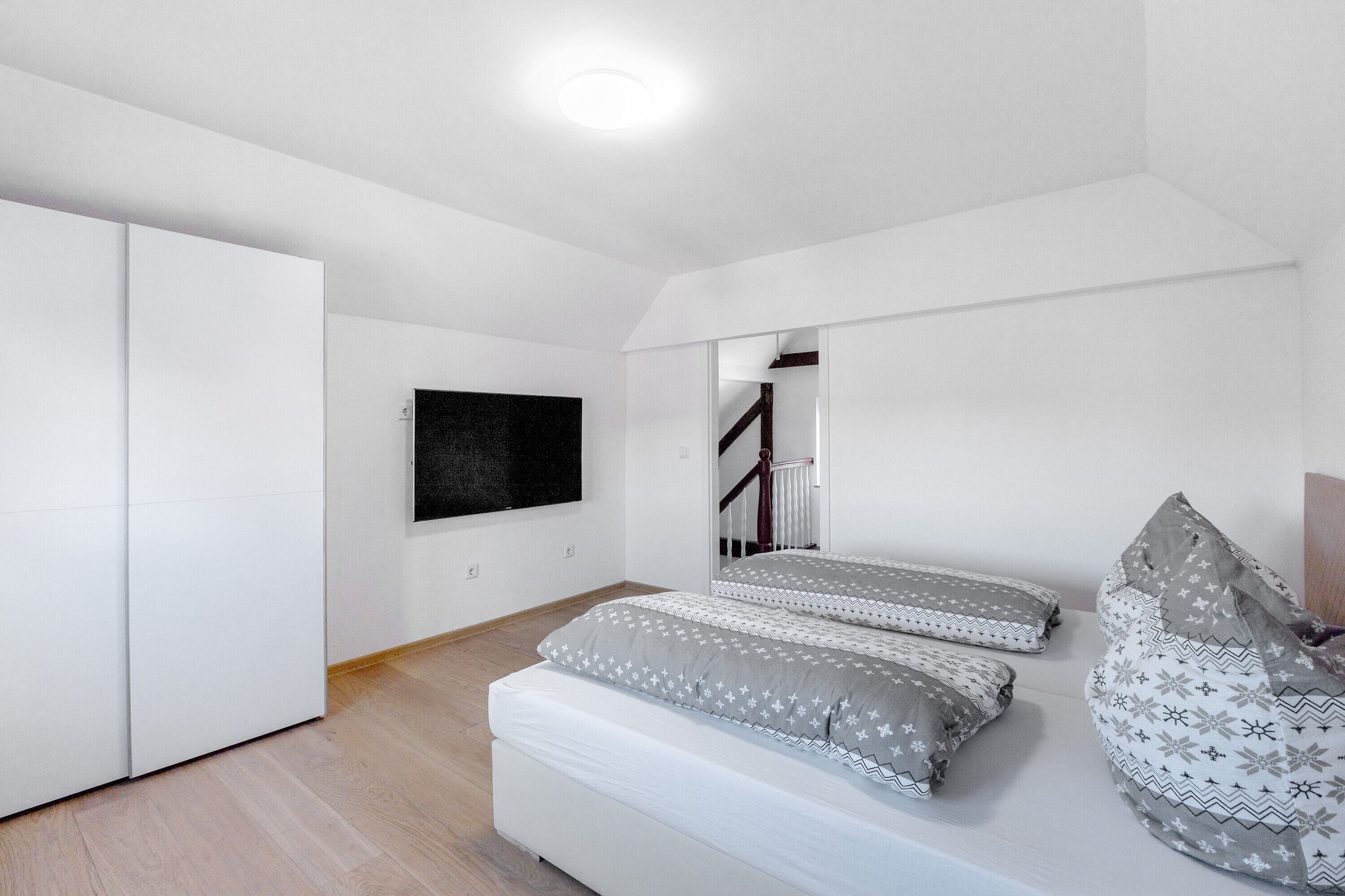 Un dormitorio con una cama, un armario, un televisor y una escalera.