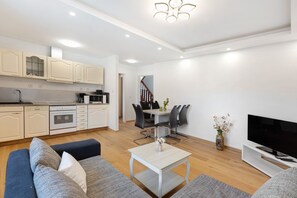 A modern kitchen with white cabinets, a dining area with a table and chairs, a sofa, a TV, and a staircase leading to another level.