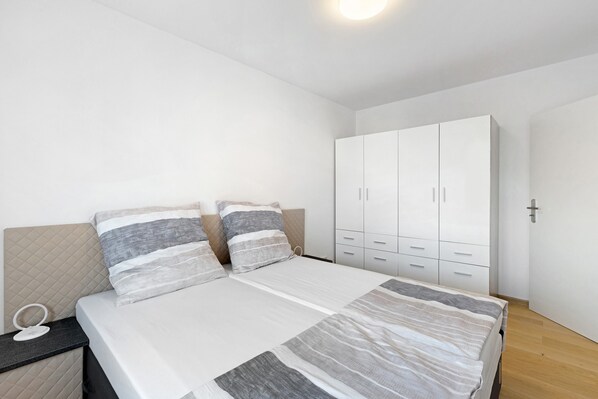 A bedroom with a bed, nightstand, wardrobe, and a mirror.