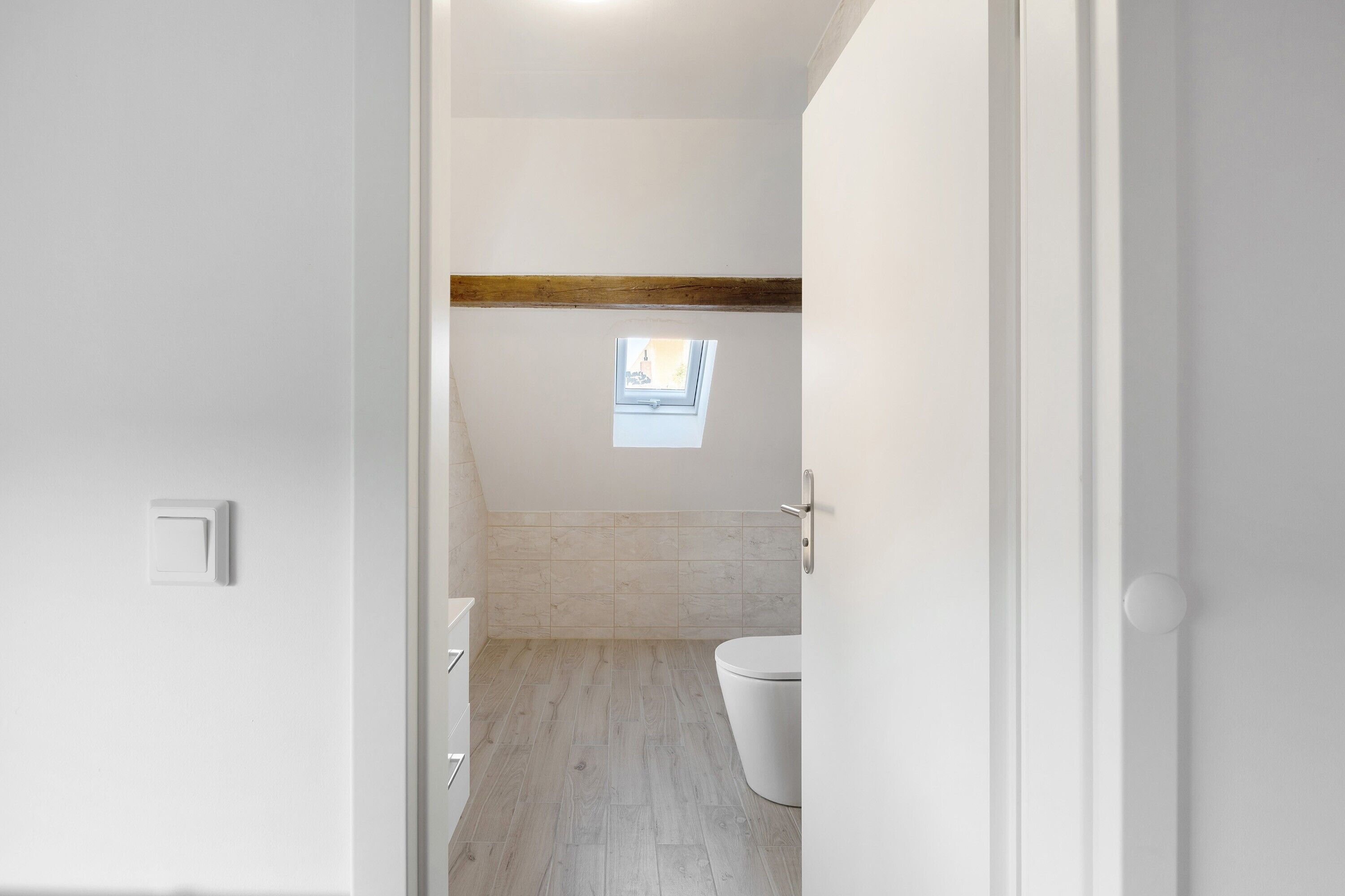 Een badkamer met dakraam, toilet en een plafond van houten balken.