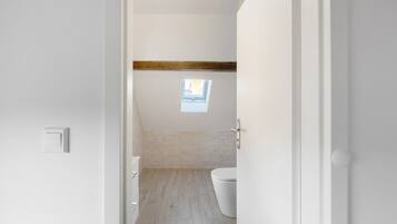 Een badkamer met dakraam, toilet en een plafond van houten balken.