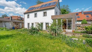 Ein zweistöckiges Haus mit Solaranlage, Garten und einer kleinen Holzkonstruktion.