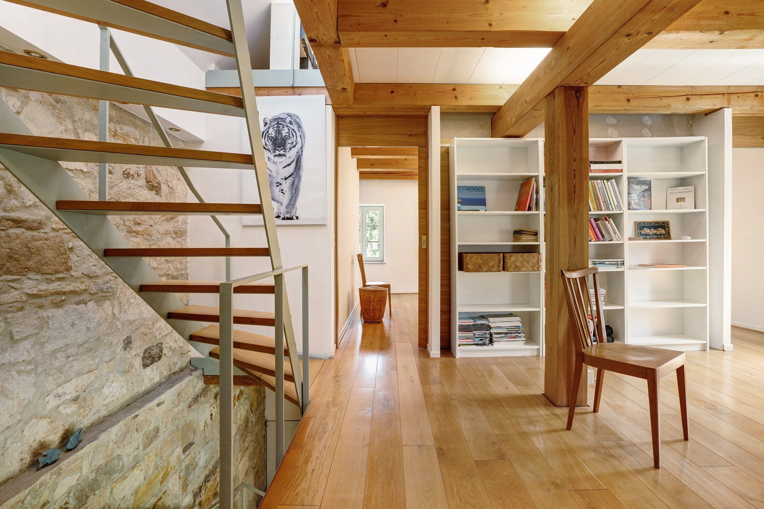 A staircase with wooden steps and metal railings, a wooden chair, and white shelving units with books and decorative items.