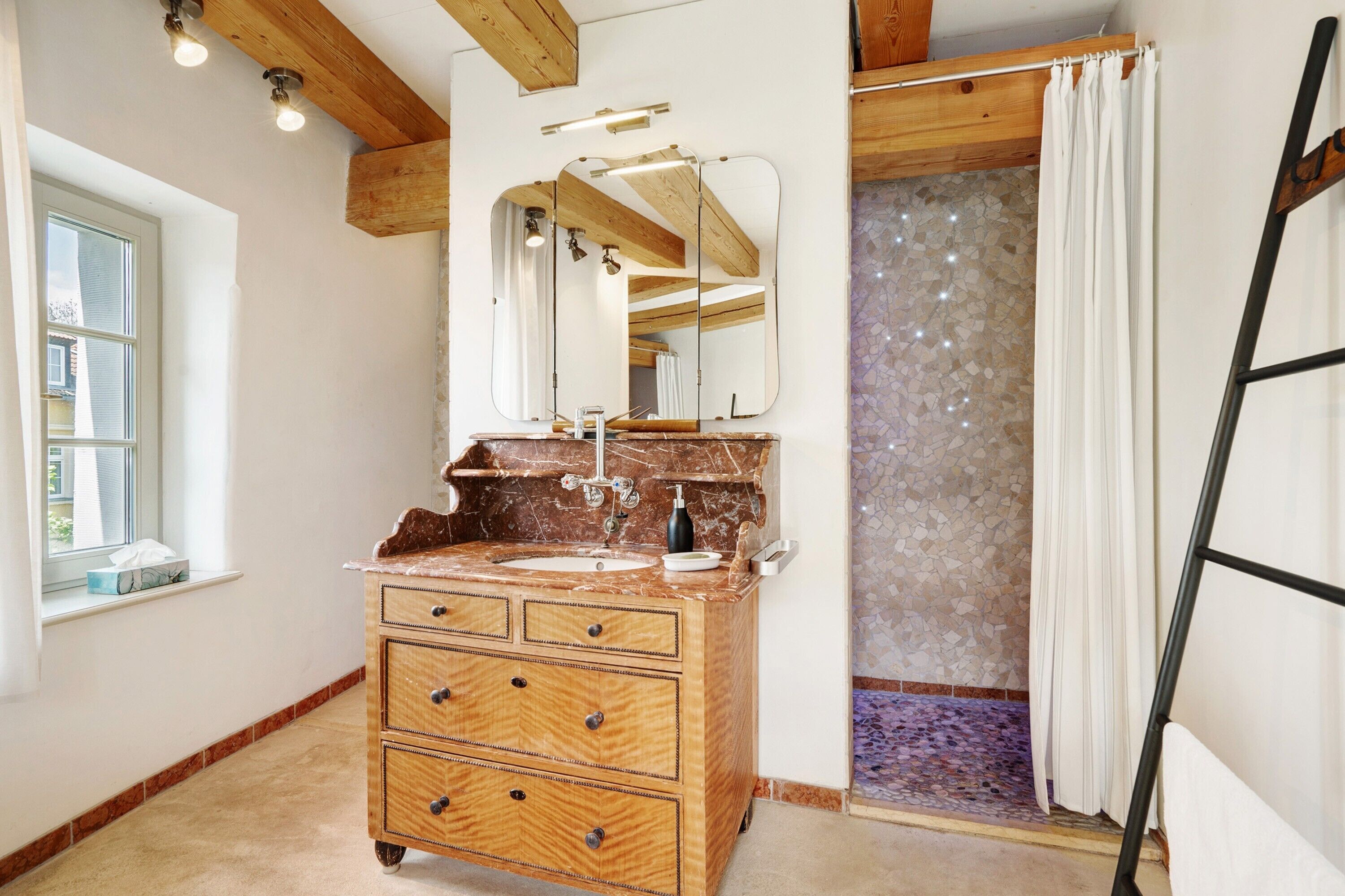 Ein Badezimmer mit einem Holzkosmetikschrank, einem Spiegel, einem Waschbecken und einer Dusche mit einer Mosaikwand.