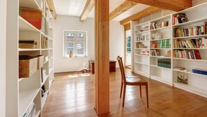 Ein geräumiges Zimmer mit Holzbalken, weißen Bücherregalen voller Bücher und einem Holzstuhl.