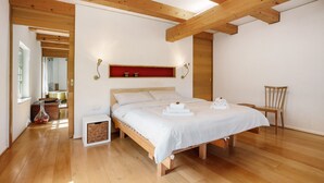 Ein Schlafzimmer mit einem hölzernen Bett, einem roten Regal, einem Sessel und einem kleinen Tisch mit einer Vase.