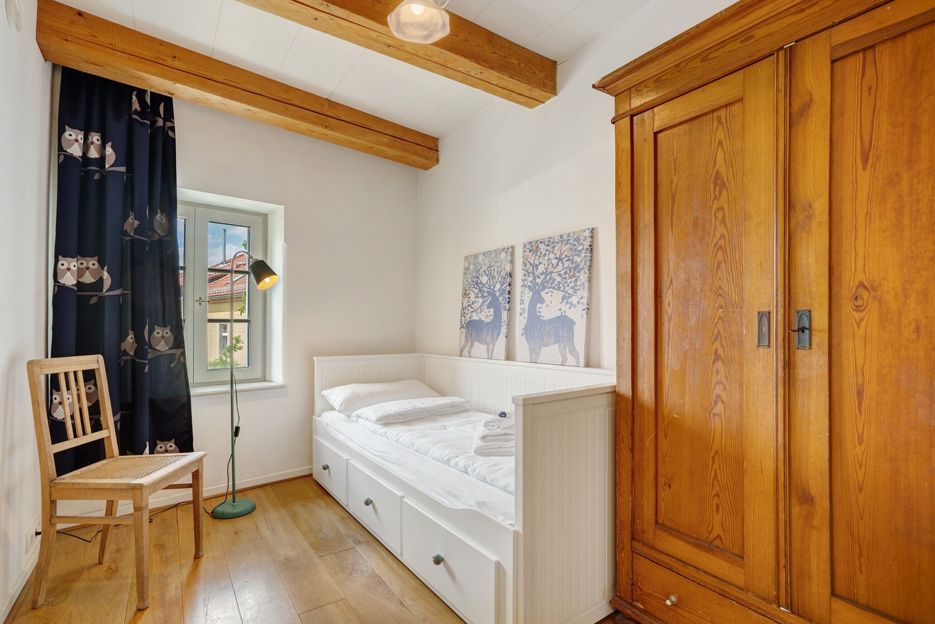 Ein kleines Zimmer mit einem Einzelbett, einem Holzschrank, einem Stuhl und einer Stehlampe.