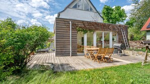 Ein modernes Haus mit einer Holzterrasse, einem Essbereich mit Gartenm öbeln und einem großen Fenster.