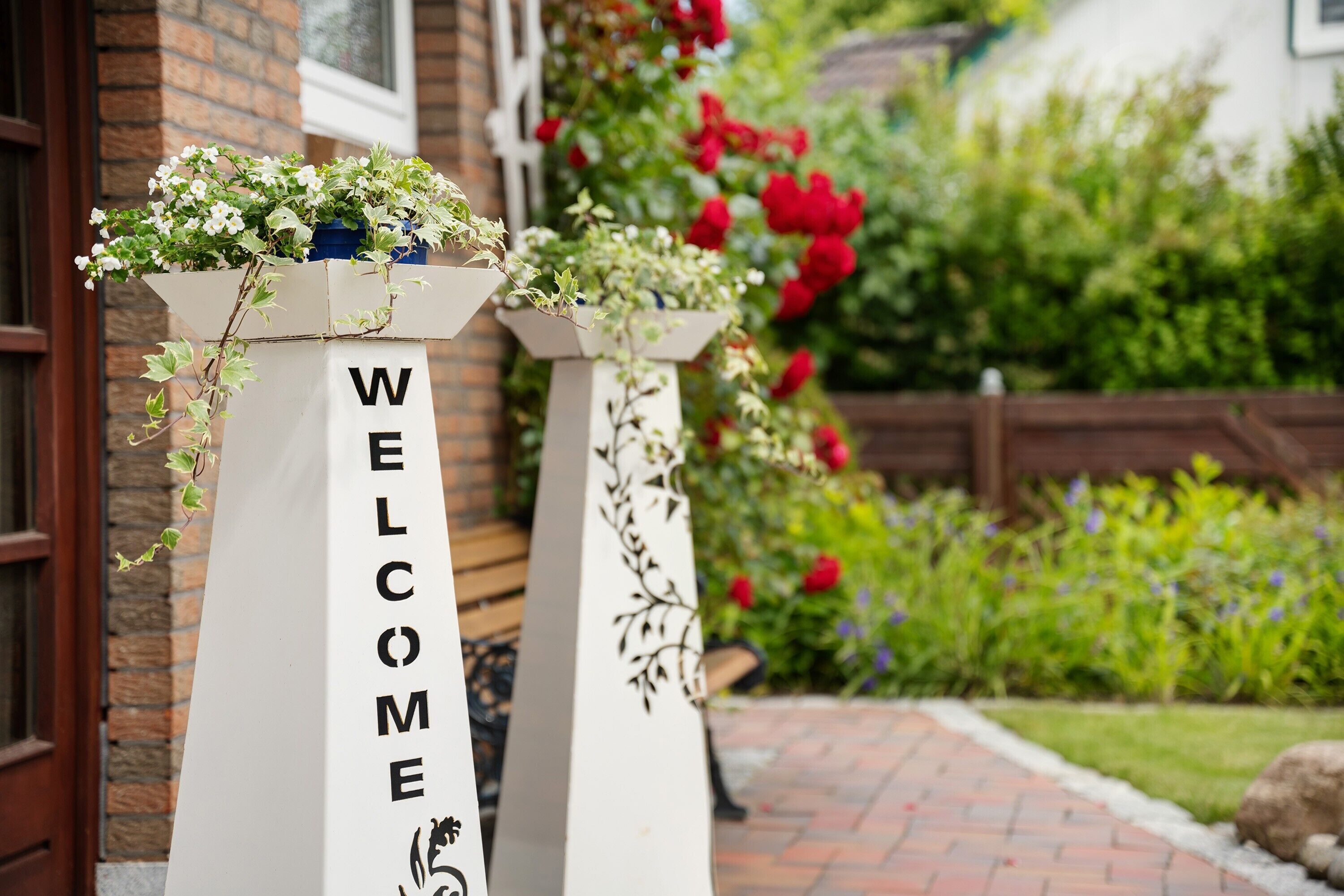 Two white pillars with 'WELCOME' written on them, each topped with a planter.