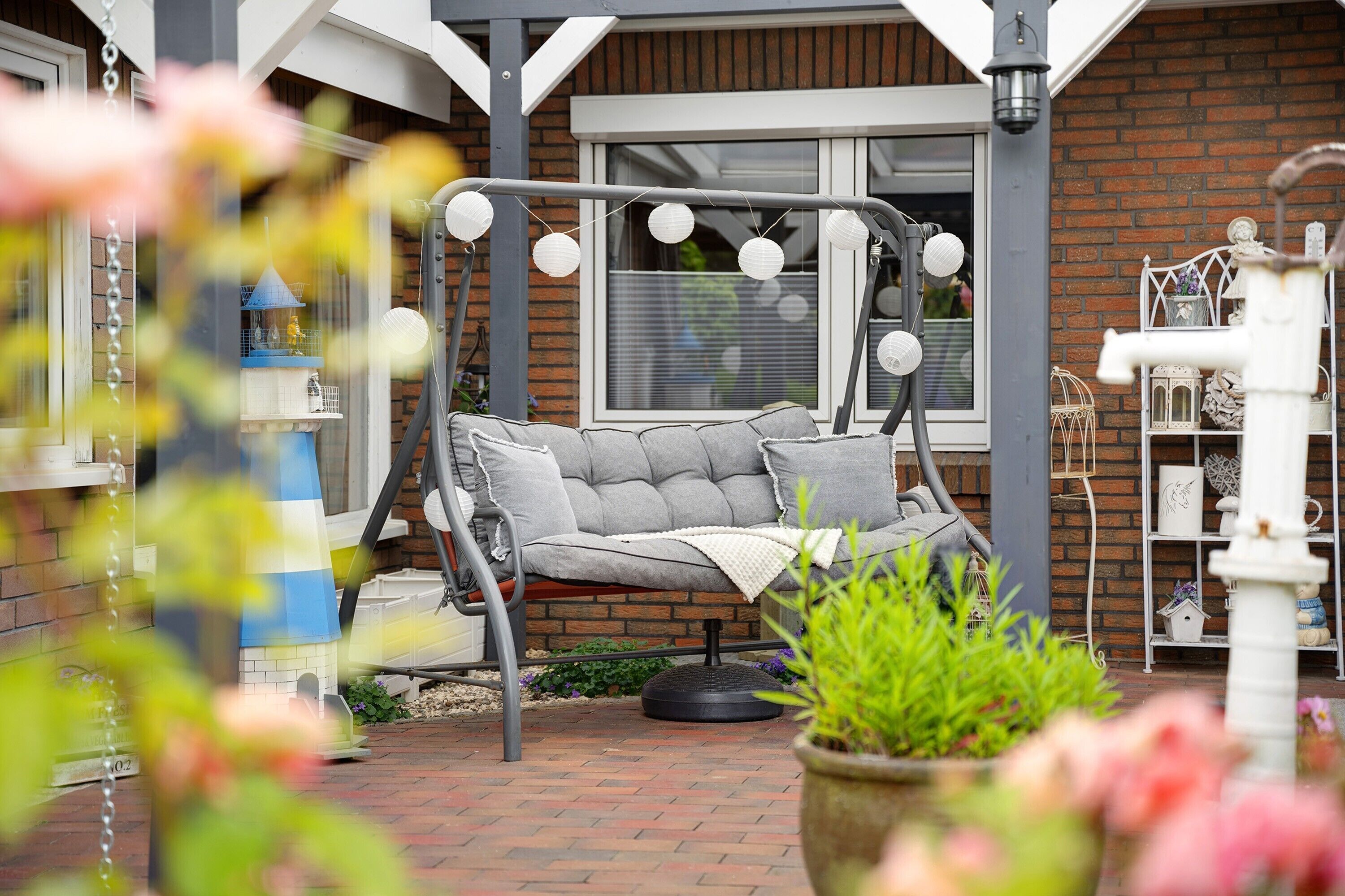 A patio with a swing chair, a bird feeder, and a white shelf with decorative items.