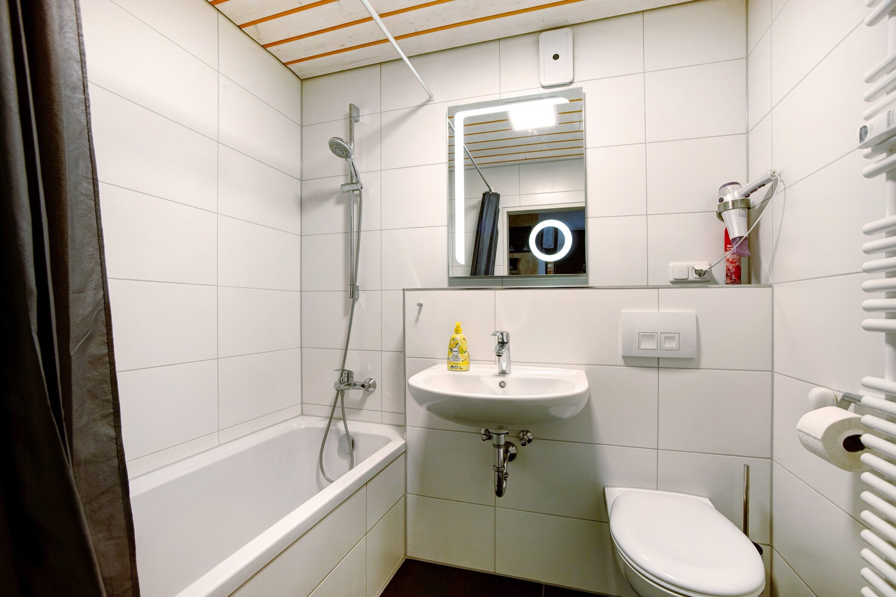 Ein Badezimmer mit Badewanne, Waschbecken, Toilette und einem beleuchteten Spiegel.