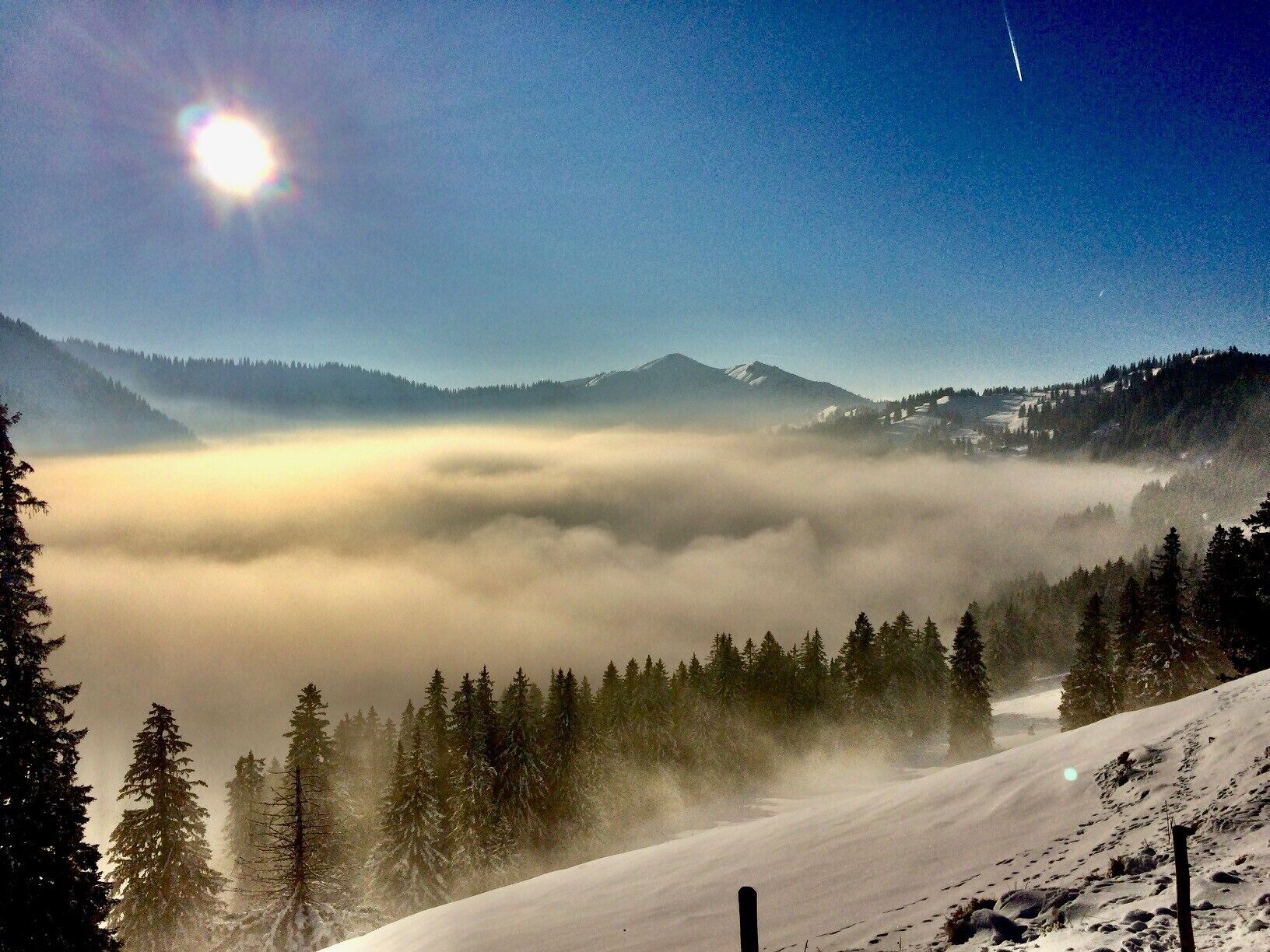 A snowy mountain landscape with a clear sky, a sunlit peak, and a forested valley.