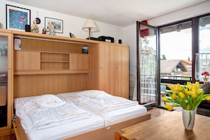 A bedroom with a bed, a wooden wardrobe, a bedside table, a vase with flowers, and a window with a view. - Apartment 'Bergrose' with Hörnerdörfer Mountain Cable Car Pass, Pool & Sauna Included (Obermaiselstein)