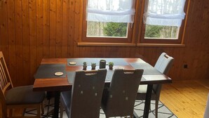 Habitació amb panells de fusta, taula de dinar, cadires i dues finestres amb cortines.