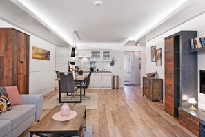 A modern living room with a sofa, dining table, and chairs, a kitchen with white cabinets, and a fireplace.