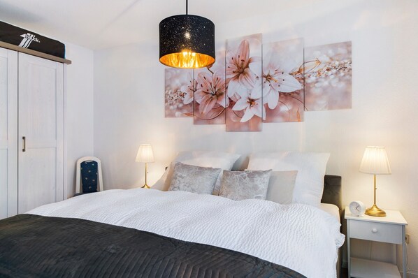 A bedroom with a bed, two bedside tables, a nightstand, a wall-mounted lamp, a ceiling lamp, and a wardrobe.