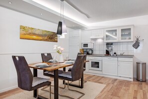 A modern kitchen with white cabinets, a dining table with chairs, and a hanging light fixture.