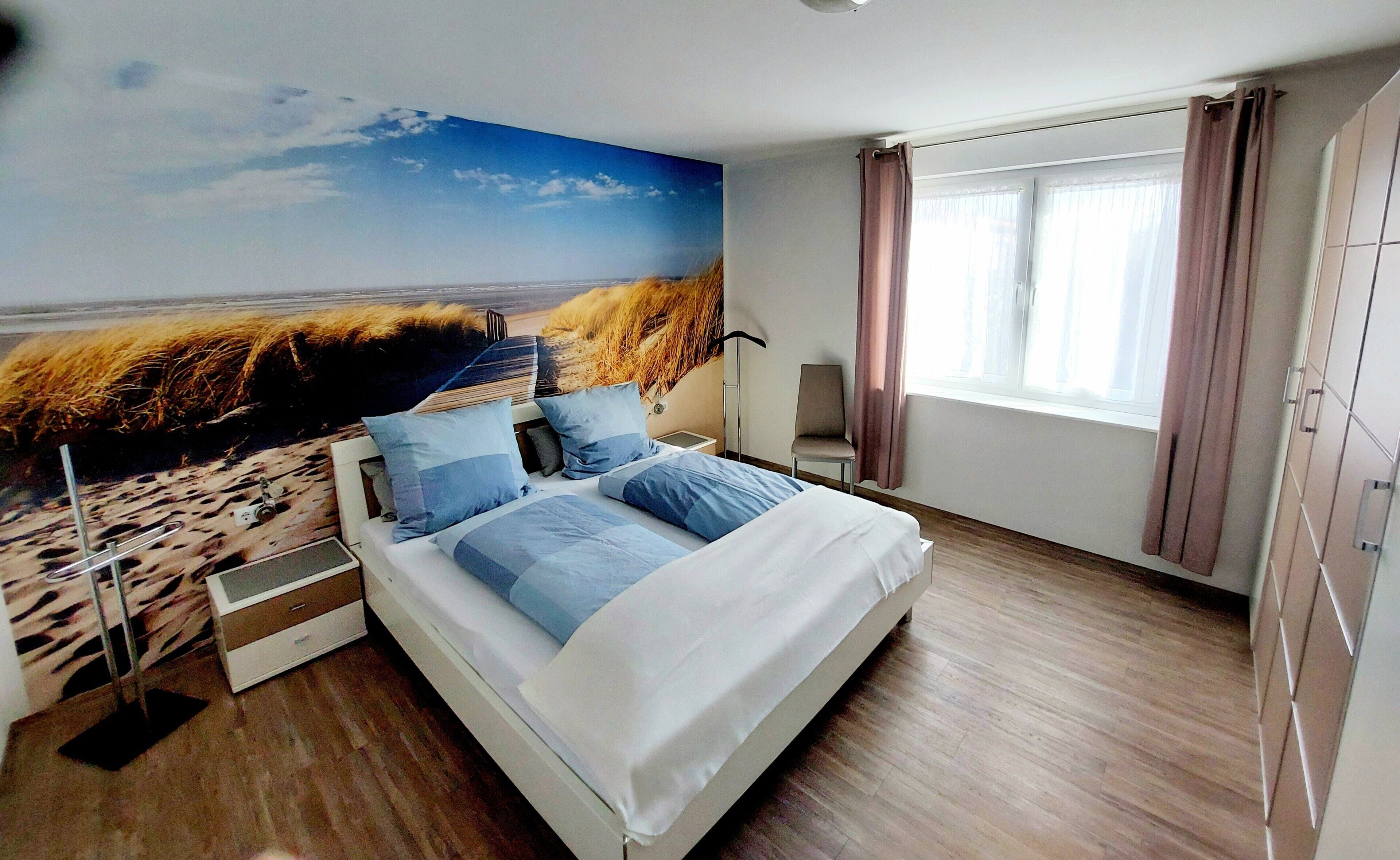 Une chambre à coucher comprenant un lit, une table de chevet, une chaise, une fenêtre avec des rideaux et une fresque murale.