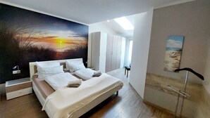 A modern bedroom with a large bed, a painting of a sunset, a wardrobe, and a desk. - Apartment 'Dünenrose' with Wi-Fi (Borkum)