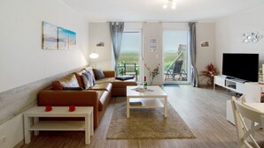 A modern living room with a sofa, coffee table, TV, and a view through the door. - Apartment 'Dünenrose' with Wi-Fi (Borkum)