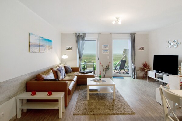 Una sala de estar moderna con un sofá, una mesa de centro, televisor y vistas a través de la puerta.
