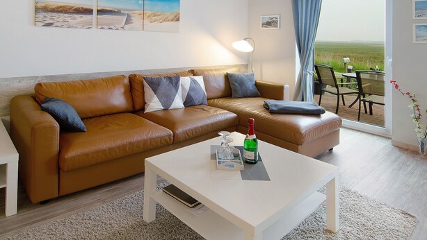 A modern living room with a brown leather sofa, a white coffee table, and a view of a grassy field through a glass door. - Apartment 'Dünenrose' with Wi-Fi (Borkum)