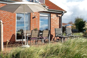 A patio with outdoor furniture, a large umbrella, and a brick building with large windows.