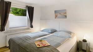 A bedroom with two beds, a radiator, a window with curtains, a bedside table with a lamp, and a tray with breakfast items.