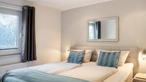 A bedroom with two beds, a window with curtains, a mirror, and a bedside lamp. - Apartment 'Sanddorn' with Wi-Fi (Borkum)