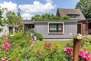En boligbygning med grå facade, et lille vindue og en have med lyserøde blomster.