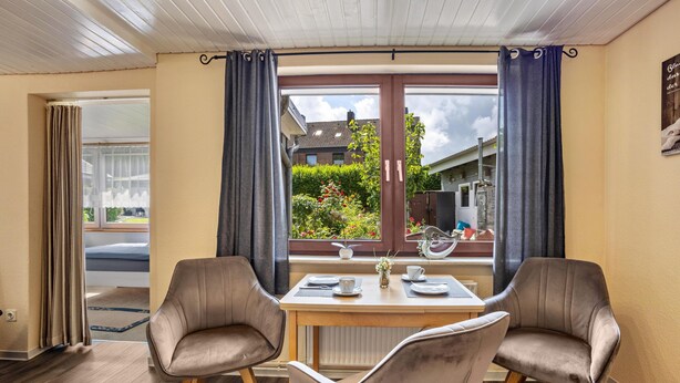 Un comedor con una mesa, dos sillas y vista a un jardín a través de una ventana.