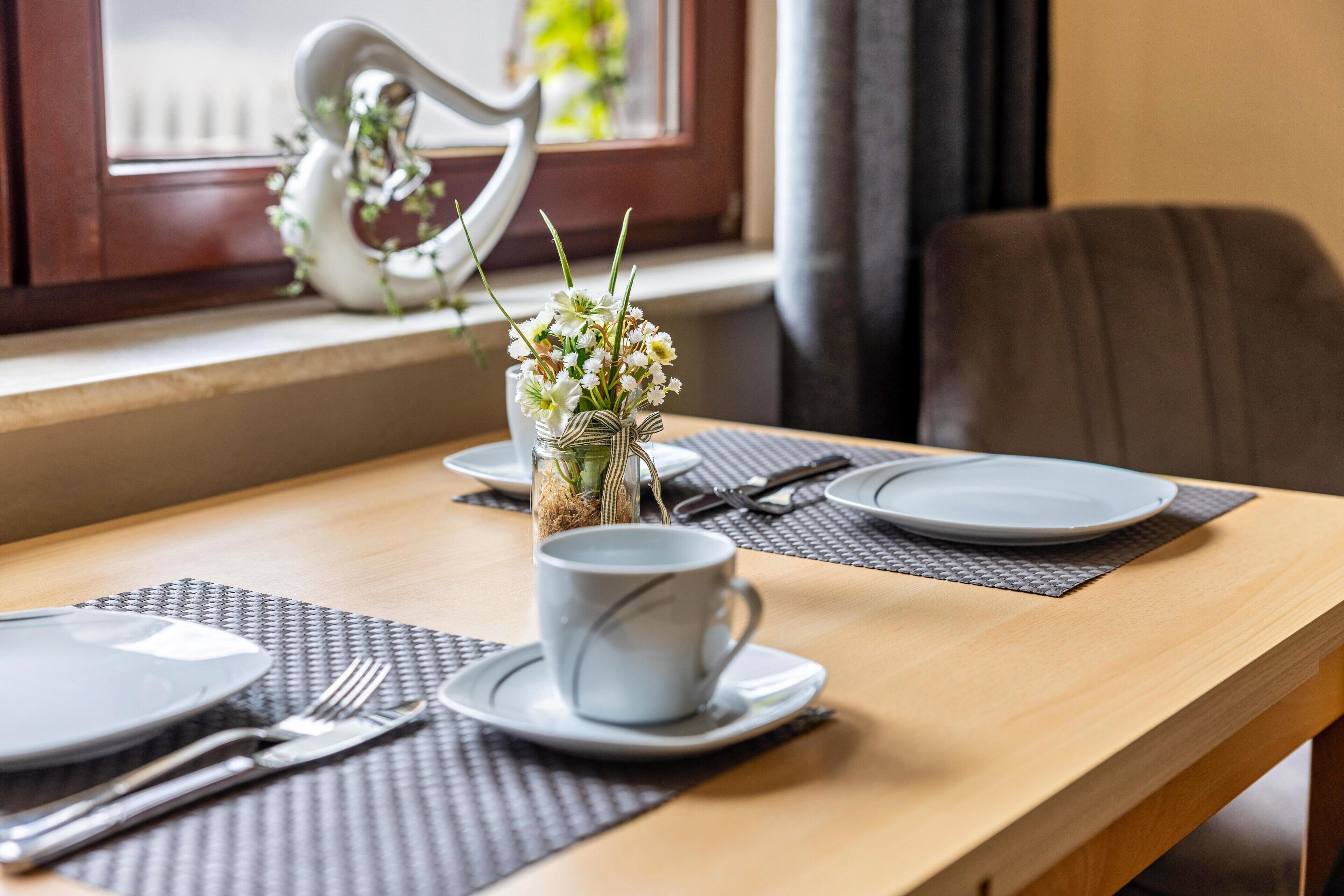 A dining table set with plates, cutlery, a cup, and a vase with flowers.