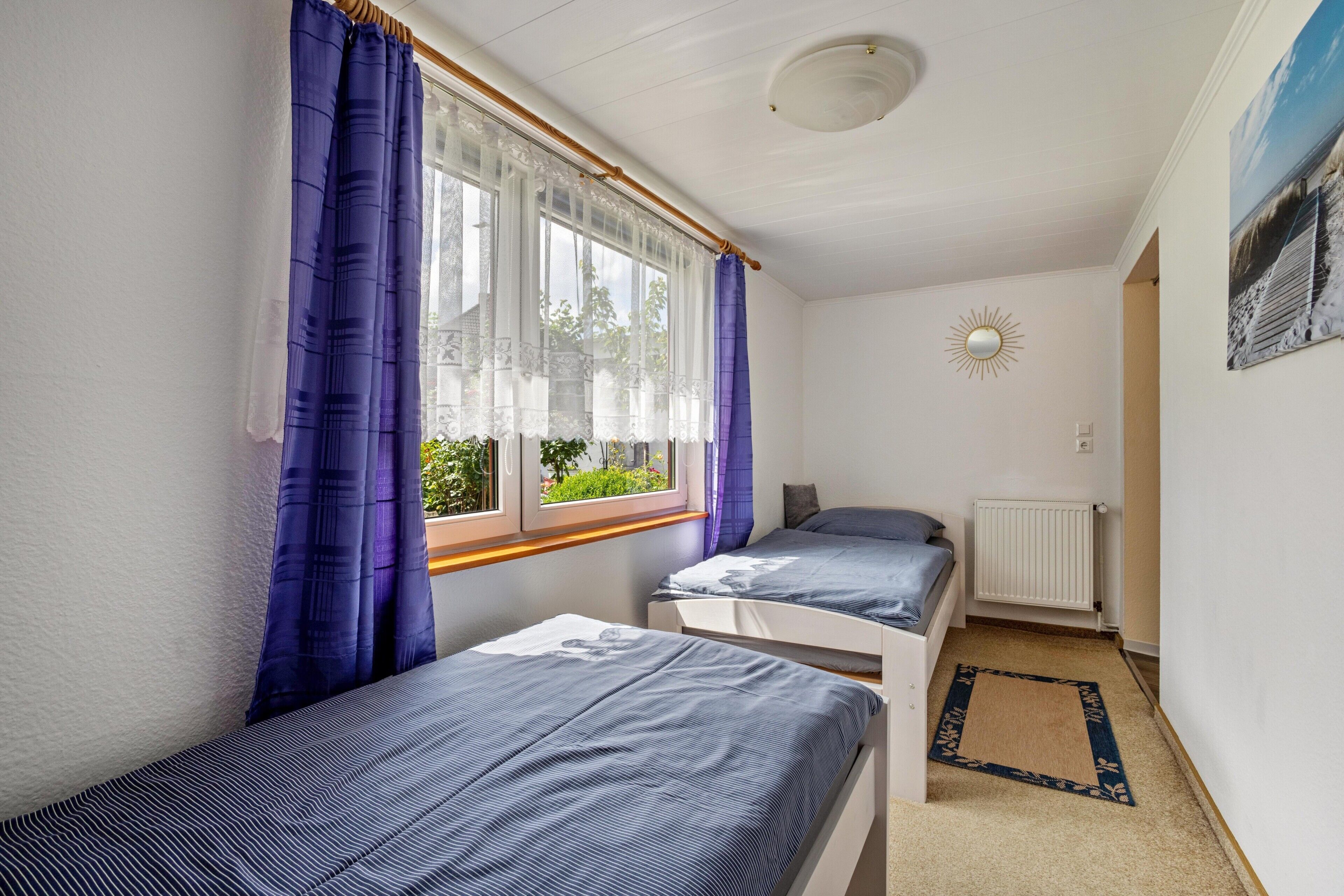 Ein Schlafzimmer mit zwei Betten, einem Fenster mit Vorhängen, einem Heizkörper und einer Sonnendekoration an der Wand.