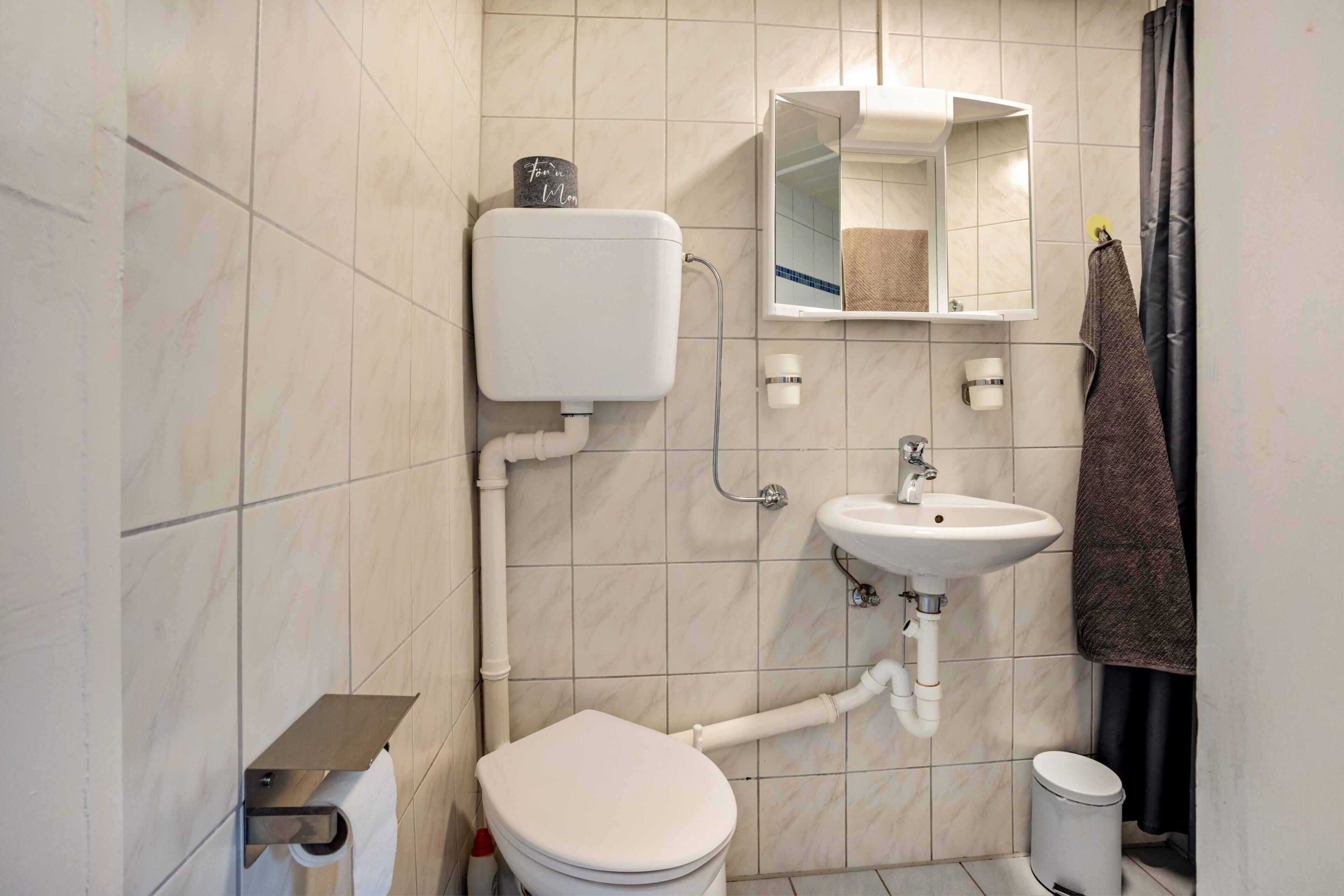 Et badeværelse med toilet, vask, spejl og håndklædestang.