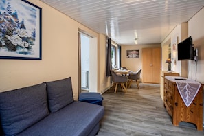 En moderne stue med sofa, spiseområde med bord og stole, et træskab og et fjernsyn monteret på væggen.