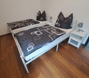 Una cama doble con colcha y almohadas de estampado geométrico, una mesita de noche con lámpara y un mueble auxiliar con cajón.
