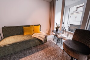 Une chambre moderne avec un canapé, un fauteuil, une petite table et une vue sur l’extérieur.