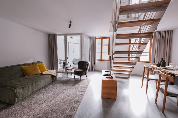 Un salon moderne comprenant un canapé, une table basse, un coin repas avec des chaises et un escalier.