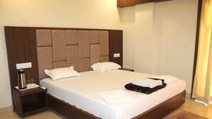A hotel room with a large bed, a nightstand with a lamp, and a brown rug. - Ashirbad Villa (Puri)