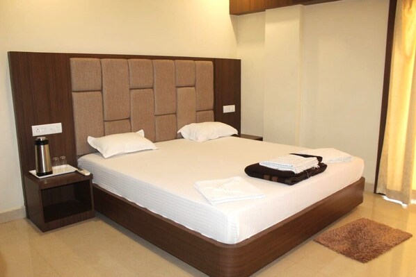 A hotel room with a large bed, a nightstand with a lamp, and a brown rug. - Ashirbad Villa (Puri)