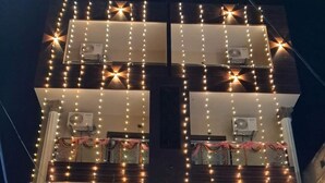 A multi-story building with balconies adorned with string lights and garlands, and the name "ASHIRBAD" prominently displayed.