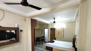 A hotel room with a bed, a sofa, a TV mounted on the wall, a ceiling fan, and a bathroom visible through an open door. - Ashirbad Villa (Puri)