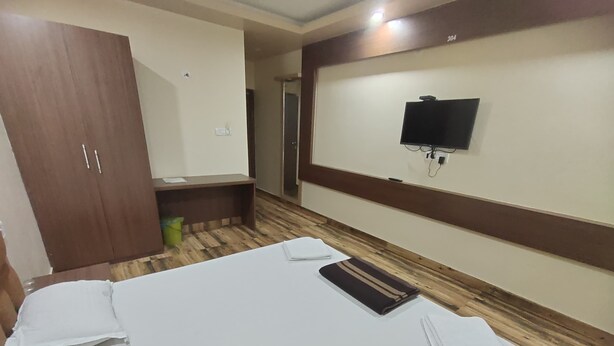 A hotel room with a large bed, a wooden wardrobe, a small desk, a television mounted on the wall, and a trash bin.